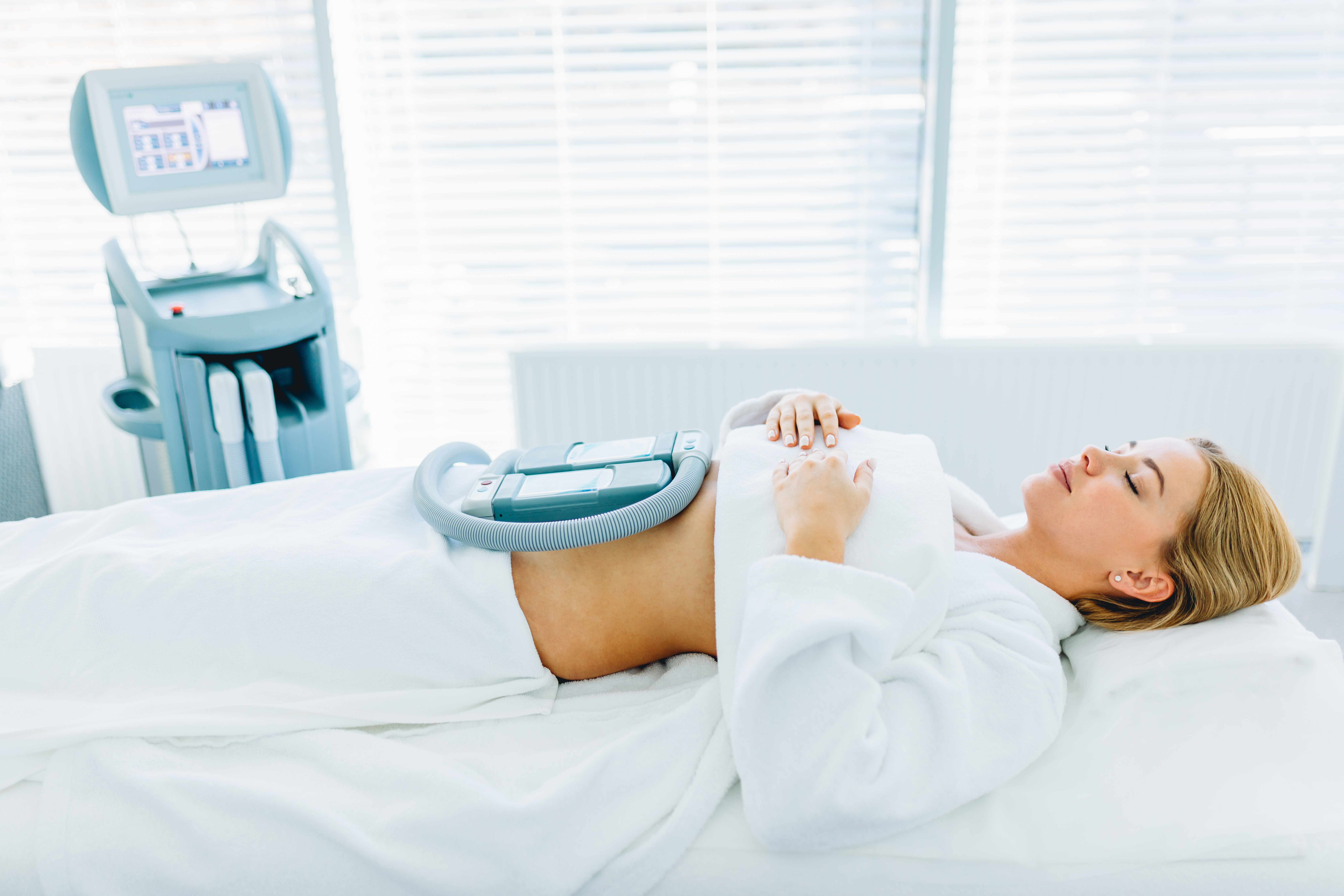 patient lies on medical table undergoing fat freezing procedure to fat reduction. Beauty vibrant massage therapy combined with crio effect gives excellent results. Body weight loss, Anti cellulite