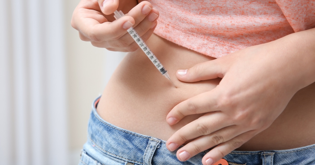 Person injecting medication into the skin of their abdomen using a syringe, with hands holding the needle and pinching the skin.